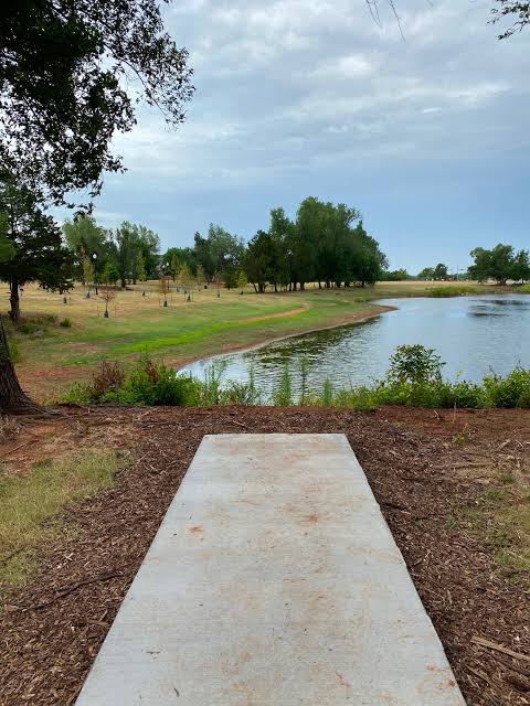 A concrete tee pad looking out over a pond toward a tree-lined fairway